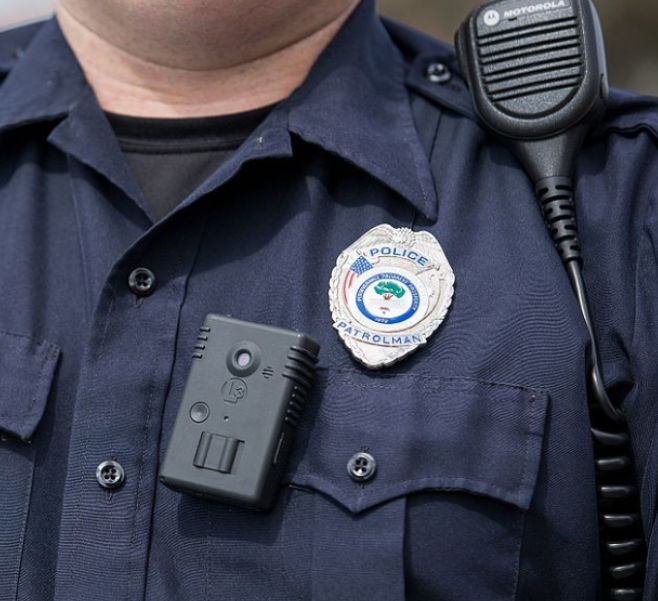 Closeup of a police officer's uniform with a badge and body camera.