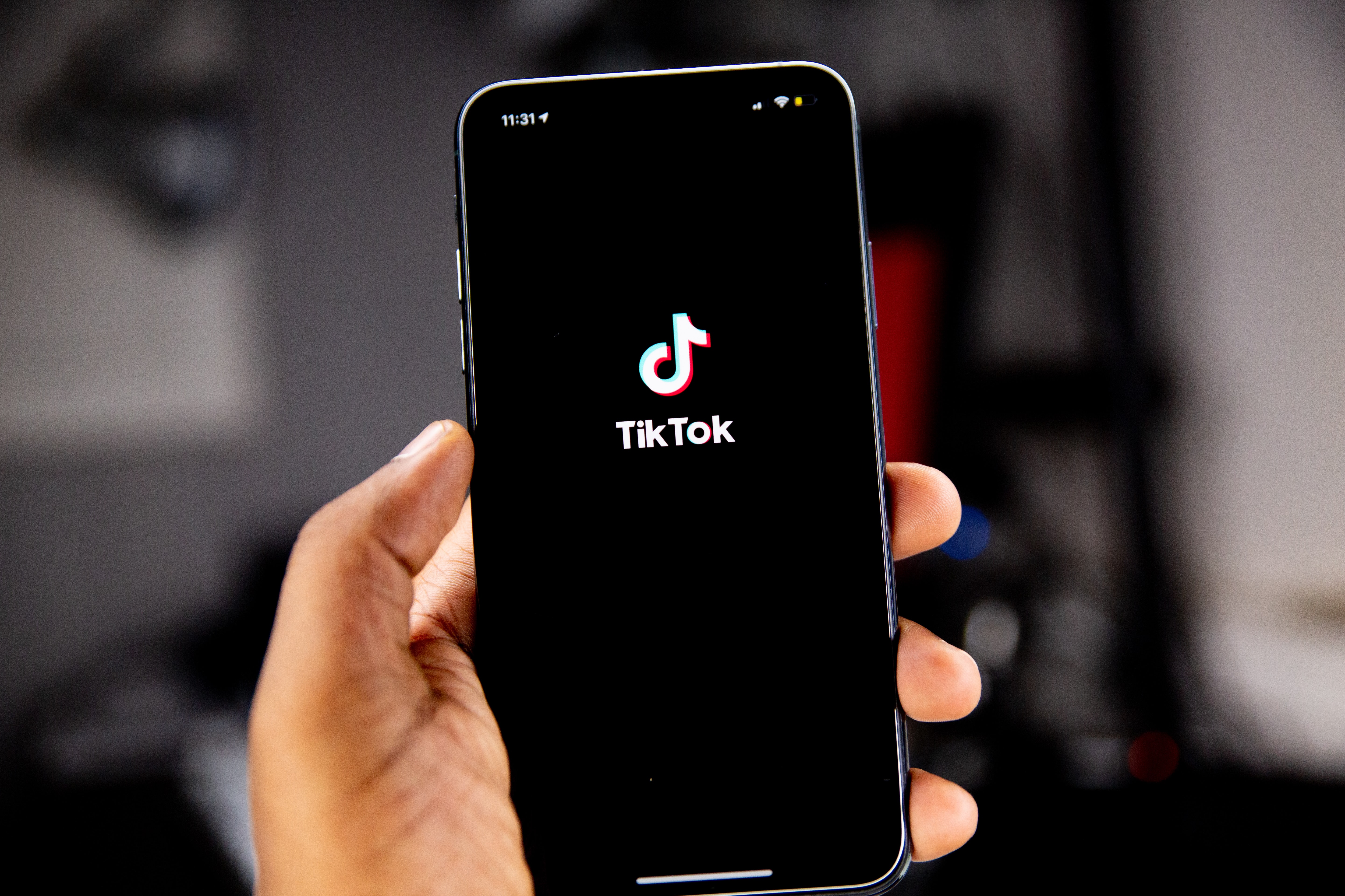 Photograph of a hand holding a phone with the TikTok logo on a black screen background