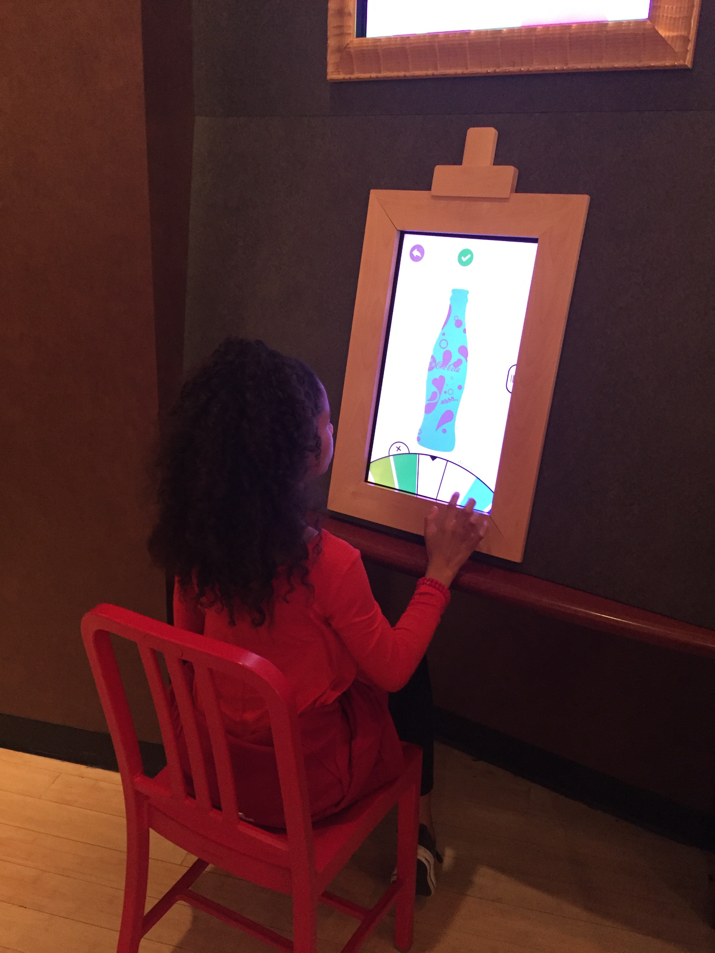 A girl sits at a computer screen designing a blue and purple bottle of Coca-Cola.