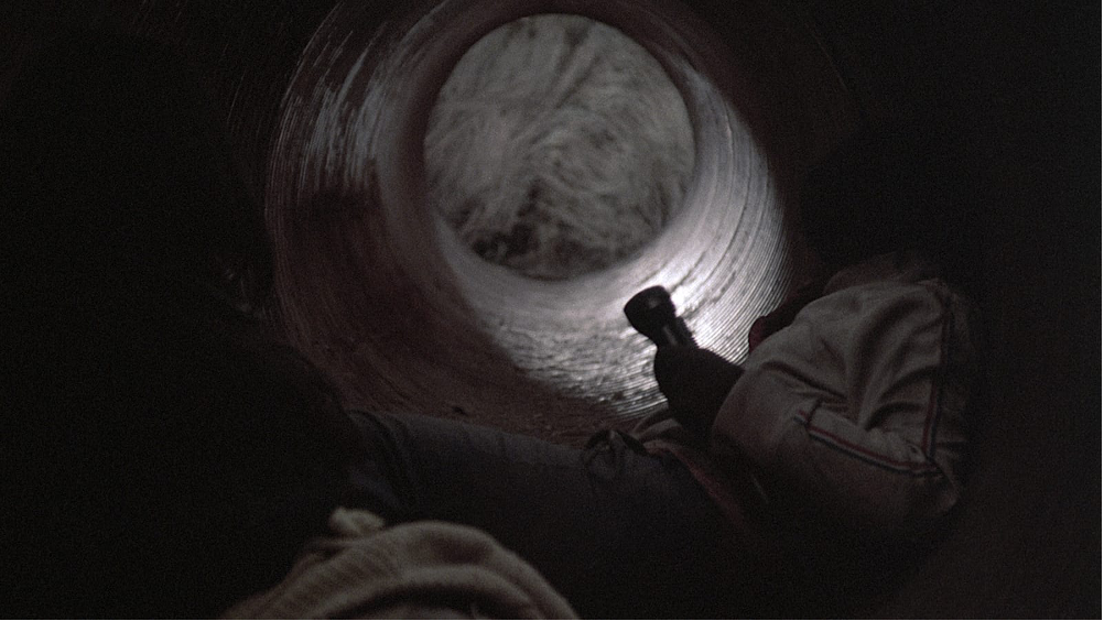 Black and white image, two people in the sewers with a fashlight