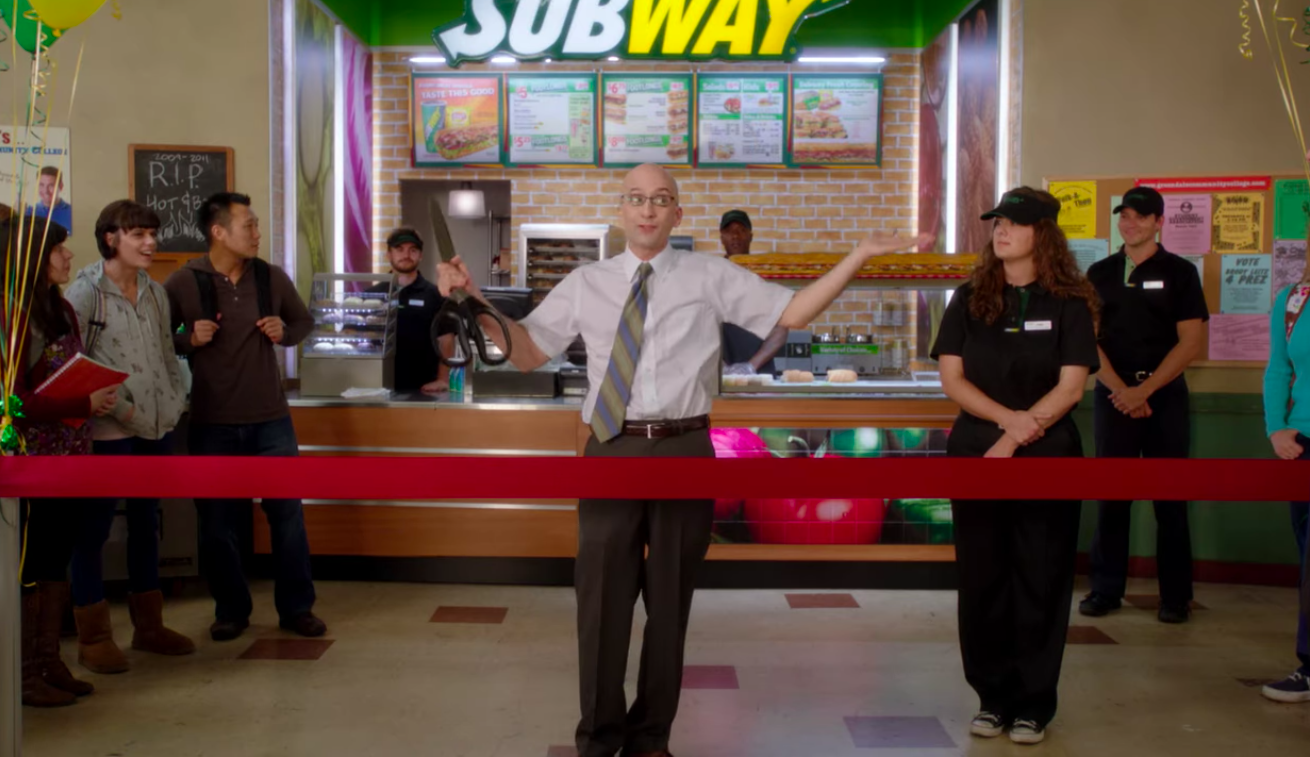 Dean Pelton from the show Community cuts the ribbon at the school's new cafeteria Subway