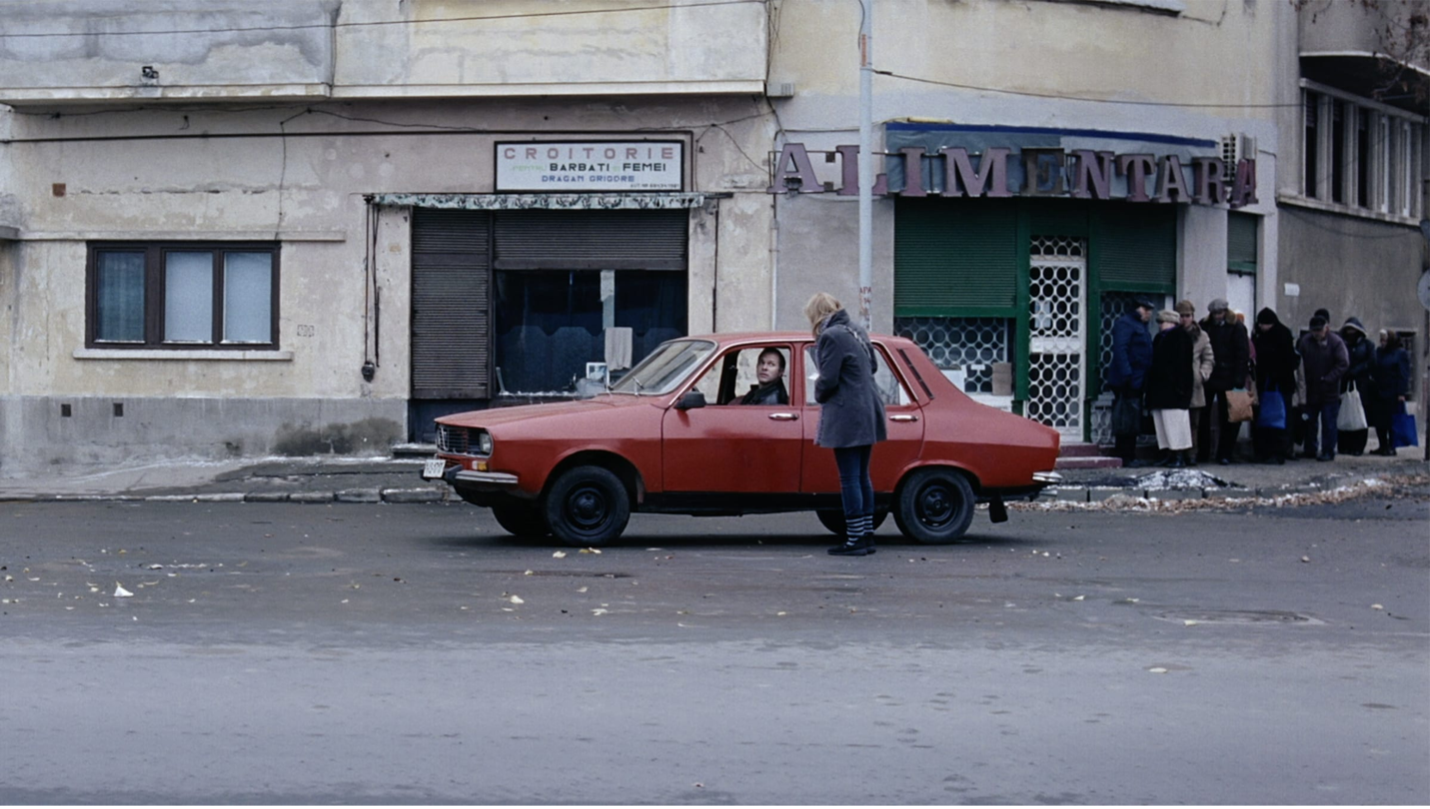 Woman standing outside of red car with a man inside from the film 4 Months, 3 Weeks and 2 Days