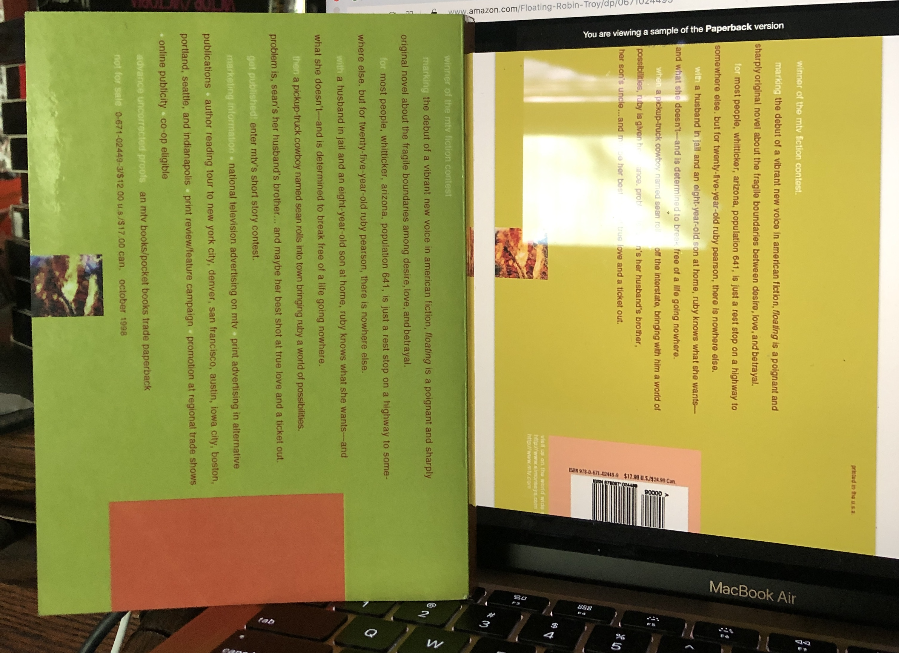 The back cover of a book next to a computer screen with the same back cover of that book on it featuring horizontal text.