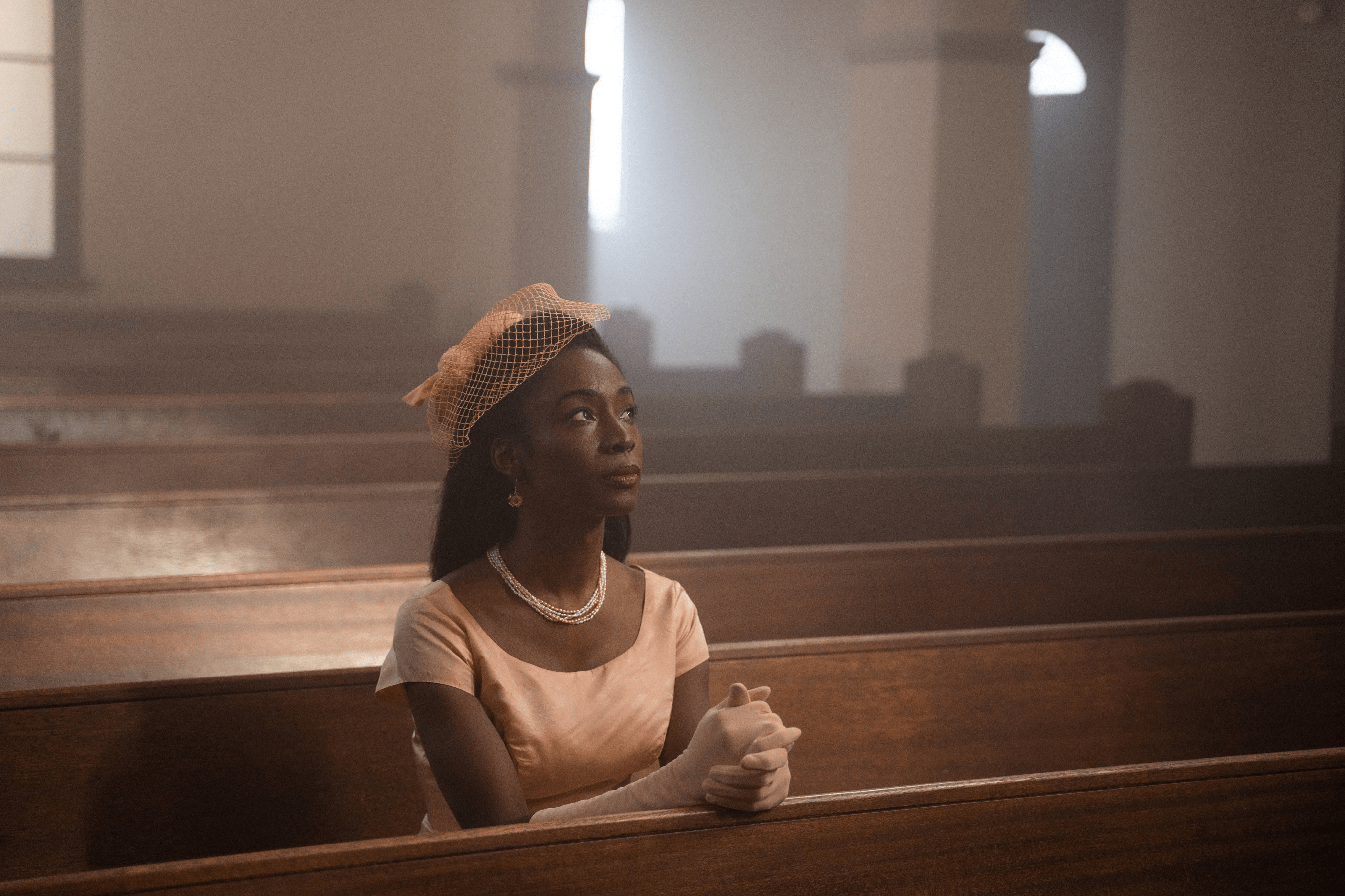 Angelica Ross is alone at a Church, sitting in a pew with hands together looking up.