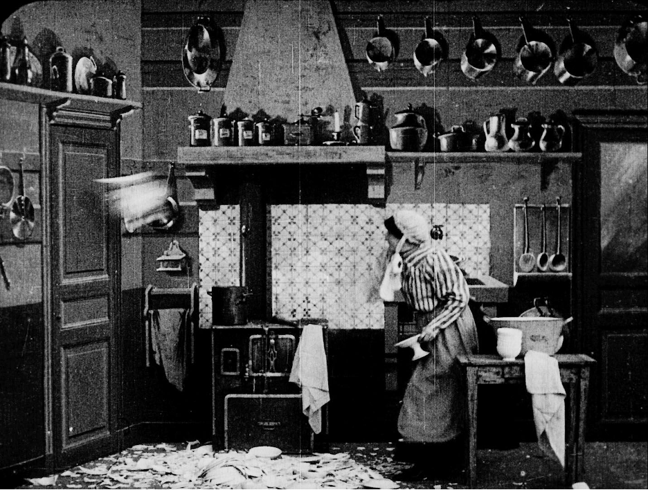 still from a black and white film in which a kitchen maid is throwing dishes against the wall