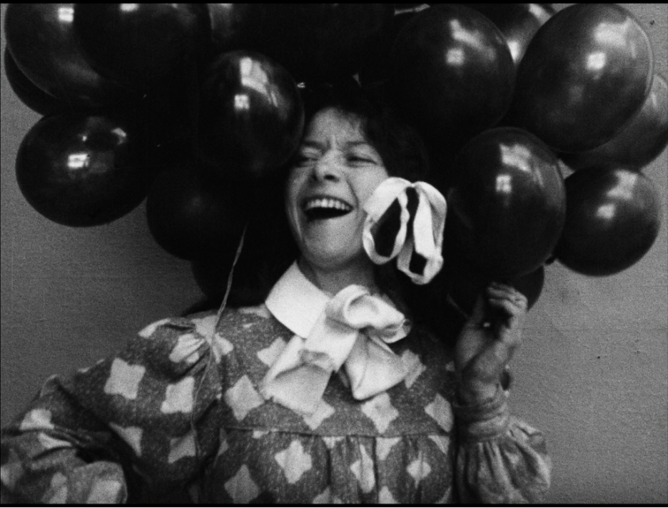 screenshot from a black and white film of a laughing girl's face, which is surrounded by balloons