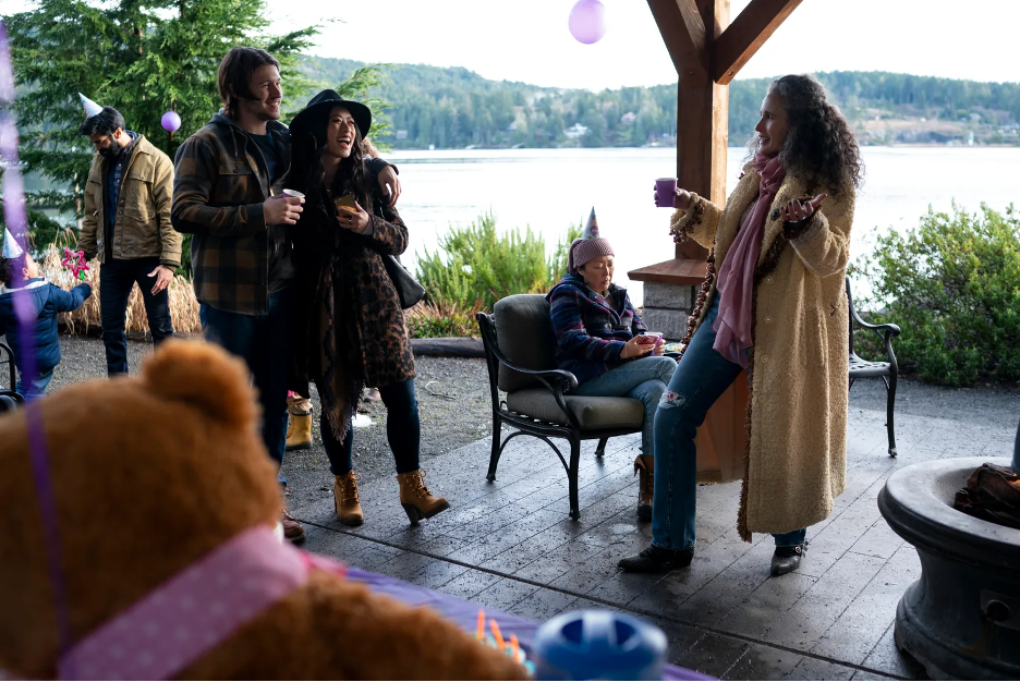 A group of adults talk at a child's birthday party inside a gazebo by a lake.