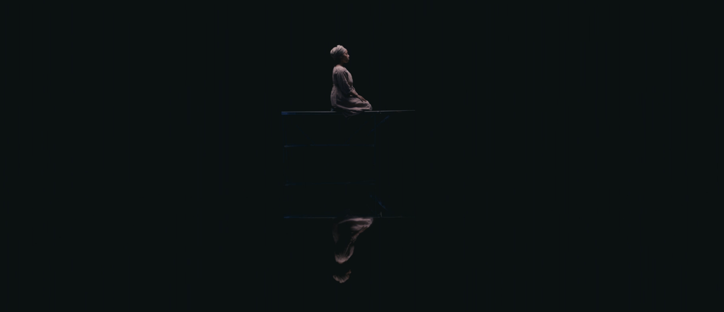 woman sitting surrounded in darkness except for her reflection below her