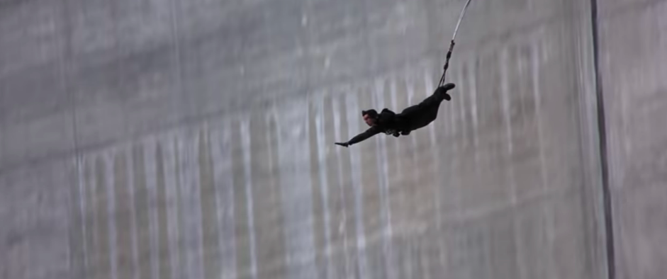 James Bond's stuntman bungee jumps down the side of the damn with his arms outstretched