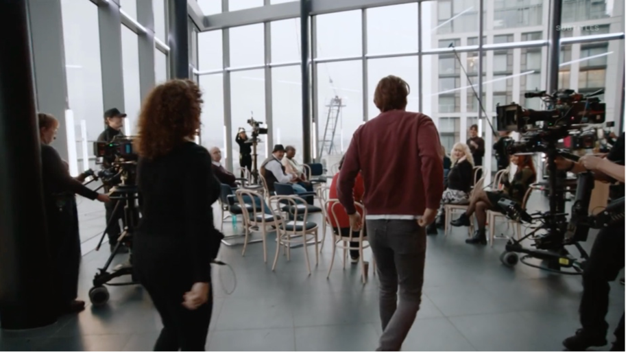 Camera operators film David Tennant as he enters a room with people sitting in chairs