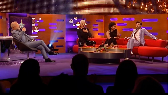 Camera operators film David Tennant as he enters a room with people sitting in chairs