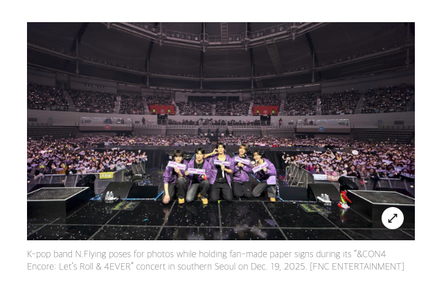 Members of BTS crouch together on stage with a crowded arena behind them